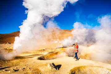 Fototapeta premium Photographer among sunshine huge steaming geysers area in Bolivia