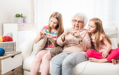 Smiling granddaughters with grandmother knitting together