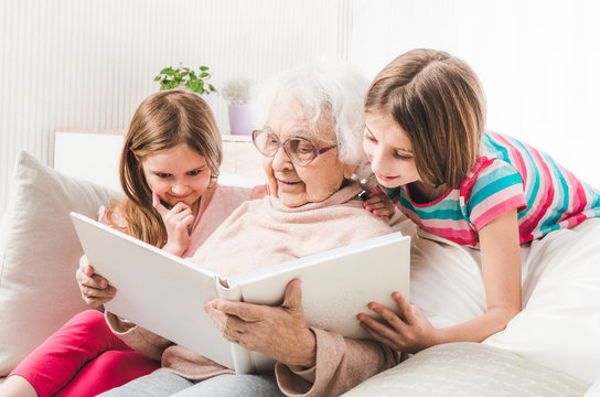 Grandmother with granddaughters looking white family photo album together