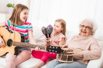 Smiling grandmother with granddaughters singing and playing on music instruments together