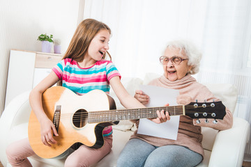 Smiling grandmother with granddaughter singing together with guitar