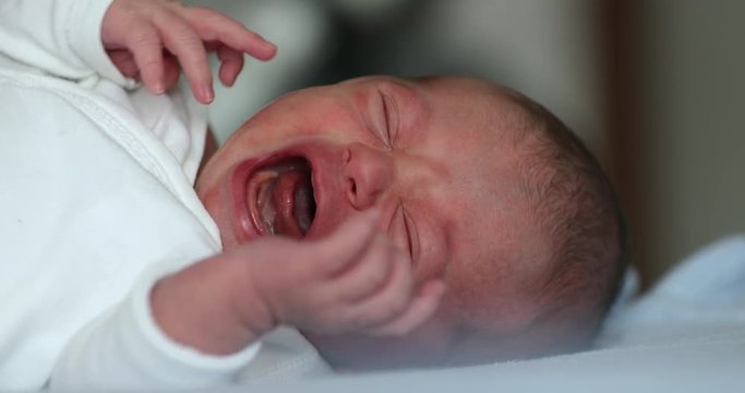 Crying newborn baby infant in first days of life lying in bed