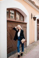 Outdoor portrait of beautiful young woman with blonde hair. Stylish girl in a black jacket and blue jeans posing on the street. Fashion model