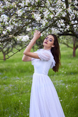 Young beautiful girl in the spring apple orchard. White lace dress on the perfect figure of the model. Fabulous image of the princess. Photo session in the open.