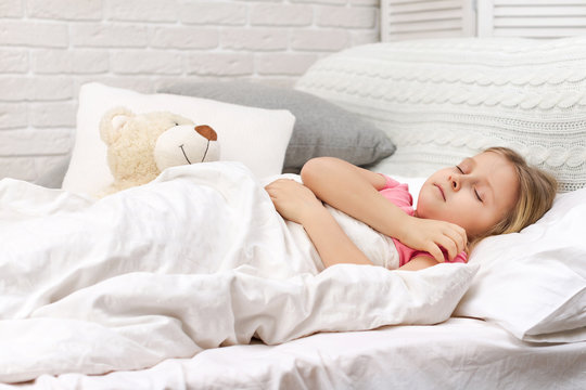 Cute little child girl sleeping with teddy bearin her bed