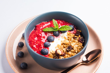 Yogurt smoothie bowl with blended raspberries, blueberries and oat matcha granola on pastel background. Delicious healthy breakfast concept