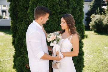 Handsome man and beautiful girl in white clothes. Couple walking outside. Bouquet of flowers