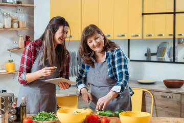 Online culinary course. Home cooking. Family leisure in kitchen. Mother and daughter watching food recipe tutorial video.