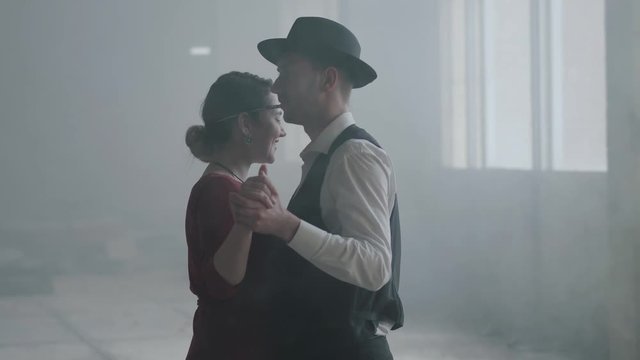 Portrait man in fedora hat, classical suits and woman in style cloth dancing in abandoned building.