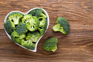 Fresh broccoli in a heart shaped bowl on a wooden background. - obrazy, fototapety, plakaty