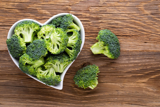 Fresh broccoli in a heart shaped bowl on a wooden background.