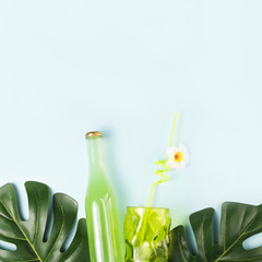 Bottle of drink near glass with straw and green plants