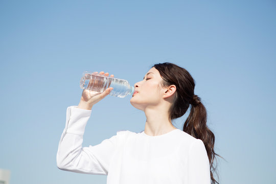 青空の下ペットボトル飲料を飲む20代女性の横顔