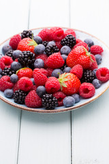 Fresh berry salad on blue dishes. Vintage wooden background.