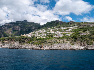 Fototapeta na wymiar Positano, Salerno, Campania, Italy, Europe - may 19 2019: view of Praiano from the sea on a boat leaving the port on Amalfi Coast. Wake of a ship with a marine village in the background