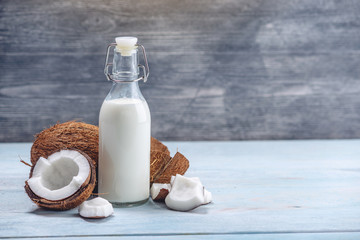 Coconut milk in a bottle with white flesh on a blue wooden background. Organic product used in cosmetology