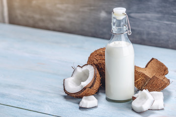 Coconut milk in a bottle with white flesh on a blue wooden background. Organic healthy product used in cosmetology