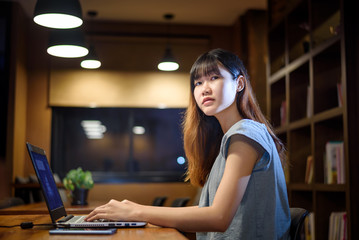 Fototapeta na wymiar Happy Beautiful Asian Student woman working on laptop in modern library room