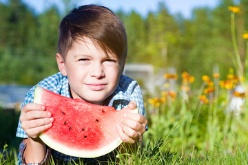 Funny boy eats watermelon outdoors in summer park