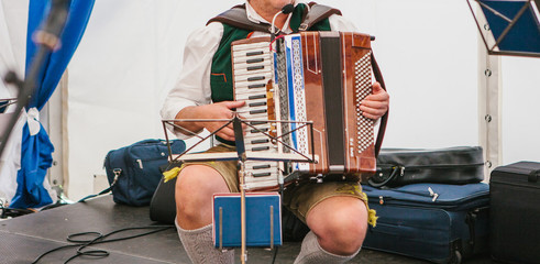 An accordionist in traditional Bavarian clothes plays the accordion on the stage. The accordionist...