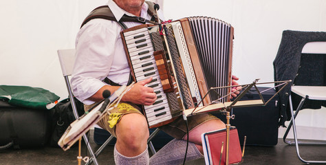 An accordionist in traditional Bavarian clothes plays the accordion on the stage. The accordionist...