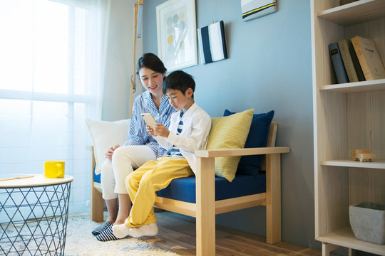 ソファに座りスマホを操作する笑顔の親子