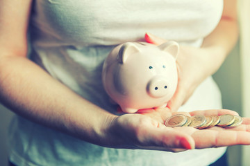 Female woman hands holding pink piggy bank and putting money Euro coin. Saving investment budget...