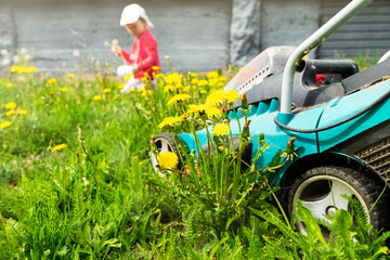 Lawn mower and in the background the child collects flowers. Garden courtyard and equipment for park maintenance. Copy space