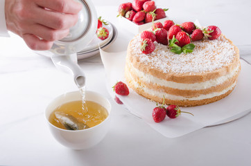 Waiter pourig hot water onto the tea bag. Tea time, delicious sponge cake with cream and fruits