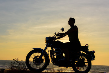Plakat Silhouette of guy on motorcycle on sunset background. Young biker are sitting on motorcycle, face in profile. Moto trip on the seaside, freedom and active lifestyle.