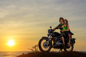 Romantic picture with a couple of beautiful stylish bikers at sunset. Handsome guy with tatoo and young sexy woman enjoy themselves in motorbike trip.