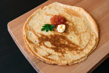 Homemade thin pancakes with red caviar on a wooden cutting board.