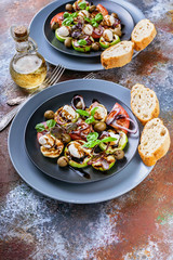 Vertical shot of italian salad with grilled vegetables, mozzarella cheese, olives, red onion, basil and balsamic sauce on a rust background. Mediterranean Kitchen. Close-up