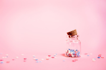 Small bottle with little stars confetti on pink background. Holyday concept.