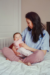 Obraz na płótnie Canvas Portrait of beautiful mixed race Asian mother holding touching embracing her cute adorable newborn infant baby. Early development and health care lifestyle concept. Family in bedroom
