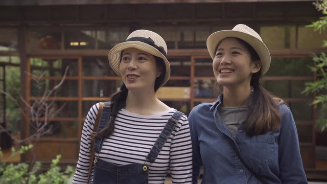 leisure friendship travel kyoto concept. happy smiling teenage girls friends walking in summer japanese style teien garden on wooden bridge outside traditional house talking chatting point view