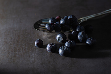 Low key blueberries on a vintage spoon and dark grey background. Stylish contemporary fresh image of healthy superfood fruit. Horizontal.