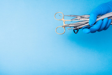 Fototapeta premium Hand in blue glove holding surgery dental tools on light blue background