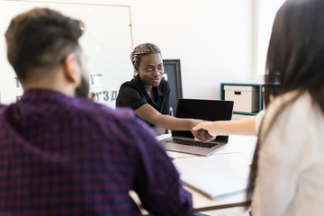 Fototapeta premium Three attractive businesspeople sitting in workplace, Young african woman handshake with new members of team in office.