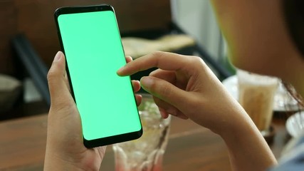 4K. woman using mobile smartphone with blank green screen mock-up at coffee shop, use finger touch on screen and slide , swiping, scrolling gestures. 