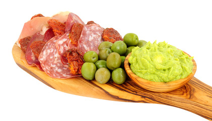 Gran antipasto snack selection on an olive wood serving board with salami, cured meat slices and a bowl of crushed avocado dip isolated on a white background