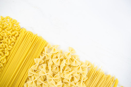 various types of pasta on a white wooden table. Italian cuisine concept, food ingredients. Flat lay. Top view, copy space