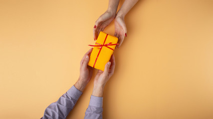 Fototapeta na wymiar man gives a girl a gift from hand to hand,box wrapped in decorative paper with a bow orange background, the concept of holidays, love and relationships, top view