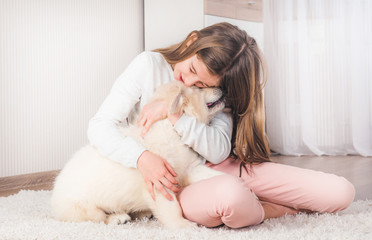 Teenage girl lying with cute fluffy retriever puppy on carpet