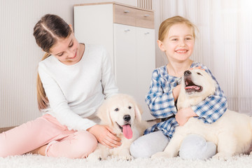 Smiling sisters sitting with cute retriever puppies on carpet