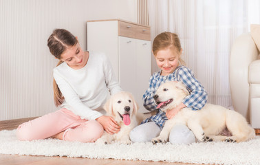 Smiling sisters sitting with cute retriever puppies on carpet