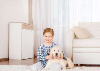 Smiling little girl sitting with cute fluffy retriever puppy at home