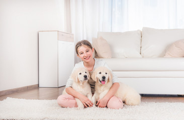 Smiling girl sit hugging cute fluffy retriever puppies on carpet at home