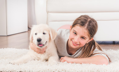 Smiling girl lying with cute fluffy retriever puppy hugging on carpet