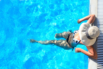 Sexy woman in bikini and sunhat relaxing in swimming pool.
